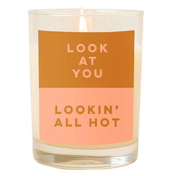 A candle with a decal that says "Look at you lookin' all hot" printed on. Top half color of the decal is light brown and the bottom half is a dusty pink. 