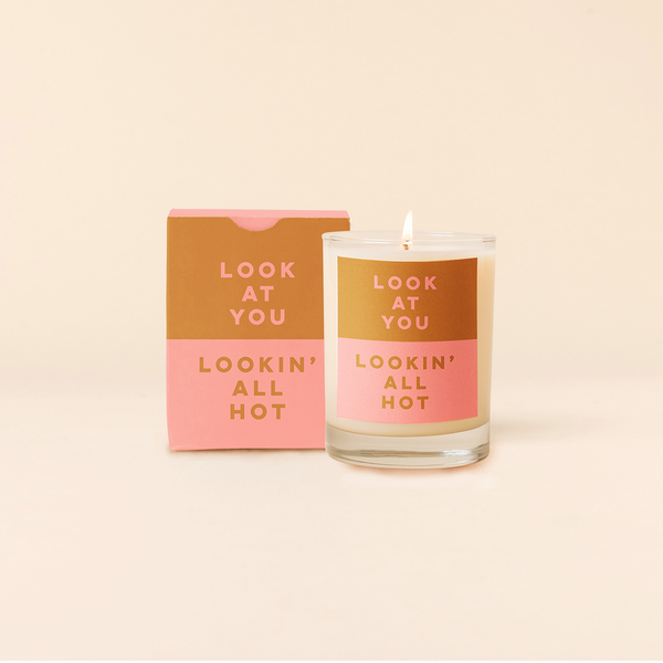 Rocks candle with two tone backdrop. Top half rust backing with pink text and bottom half pink backing with rust text reading "LOOK AT YOU LOOKIN' ALL HOT". Two tone box packing with same text as candle.