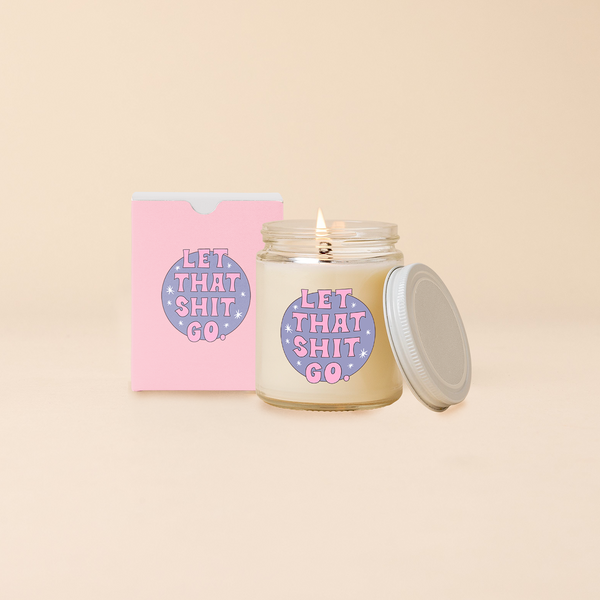 Glass jar candle reading "LET THAT SHIT GO" in front of purple circle backdrop with minimal star design. Box packaging with same design as candle. 