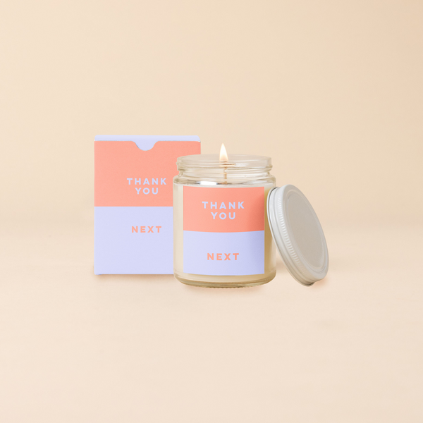 An 8 oz. candle w/ a lid and a split-colored decal (Peach and Lilac) and the phrase, "Thank you next" printed on.