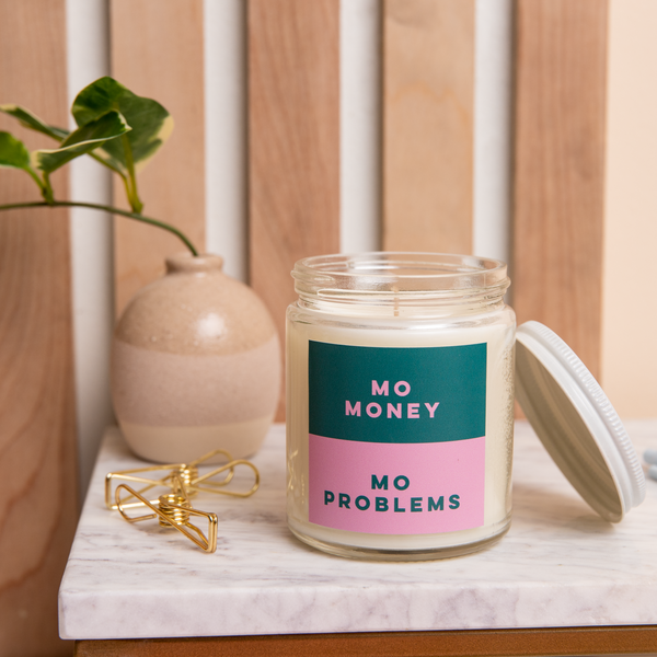 An 8 oz. candle w/ a lid and a split-colored decal (Green and Pink) with the phrase, "Mo money mo problems" printed on.