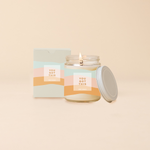 Jar candle with lid; Blue, peach, and orange wavy print wraps around the jar with text that reads "YOU GOT THIS" on the front of the candle. Box packaging with same design sits behind candle.