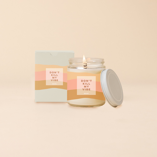 Jar candle with lid; Pink, peach, and orange wavy print wraps around the jar with text that reads "DON'T KILL MY VIBE" on the front of the candle. Box packaging with same design sits behind candle.