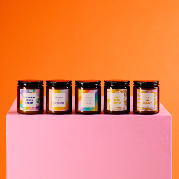 Amber candle jars with lids and delightful sayings lined up on a pink pedestal. 