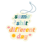 "Same Shit Different Day" air freshener with cool tone and warm letter print including stars, moon, sun, and clouds around.