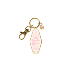 Gold key charm in the shape of a motel key holder with a baby pink background. In a slightly lighter pink "No Fucks Given" is printed while "No Vacancy" in below it. The words "Welcome To The Motel" in gold surround "No Fucks Given."