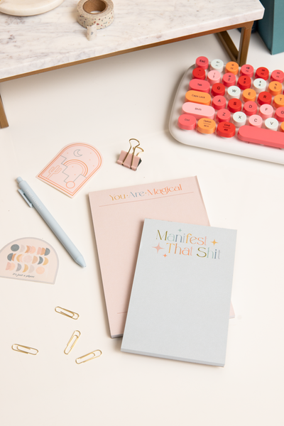 Small notepads in pale pink/"you are magical" and pale blue/"manifest that shit" 