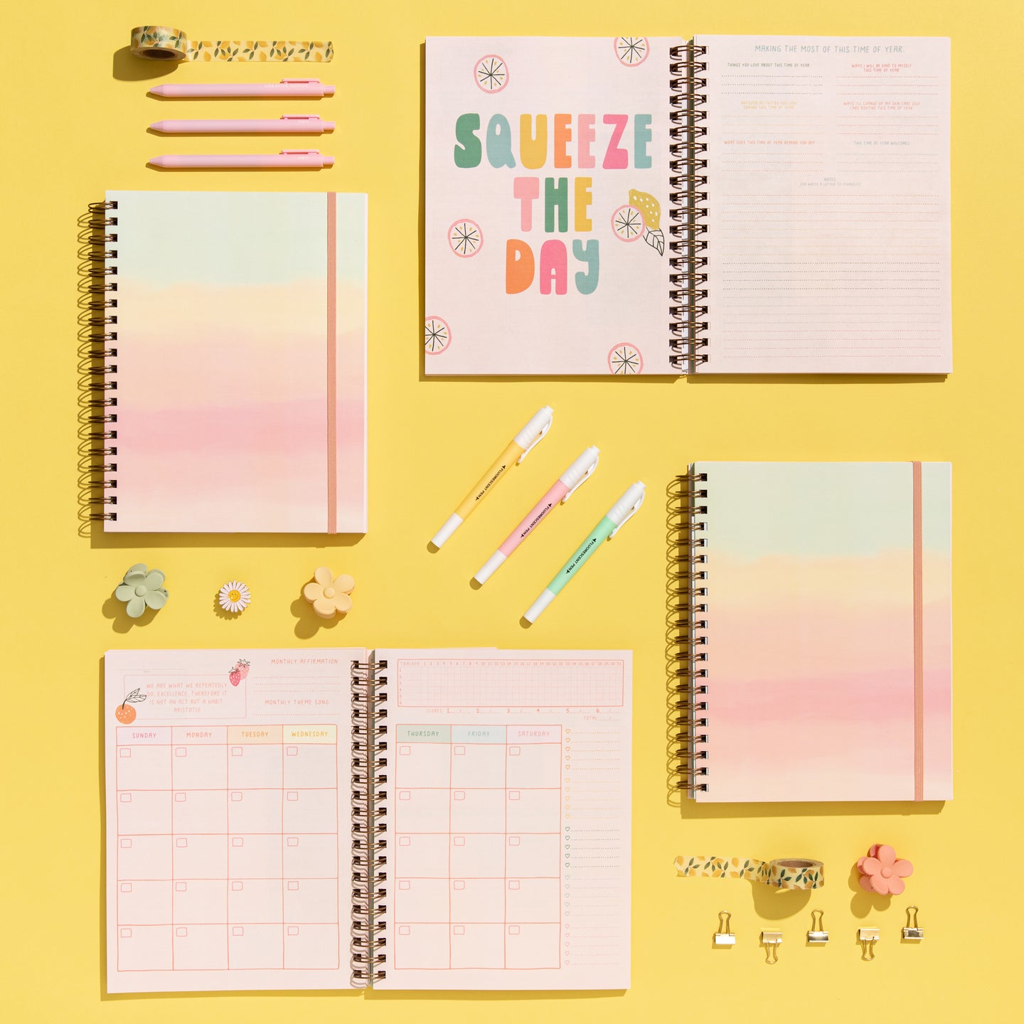 A bright and cheerful flat lay of spiral-bound planners and stationery on a yellow background. Centered is an open planner with the phrase “SQUEEZE THE DAY” in colorful block letters. Surrounding items include pastel gradient planners, open monthly calendar pages, pastel highlighters, pink pens, washi tape, binder clips, and daisy and flower-shaped accessories—creating a vibrant and motivational workspace.