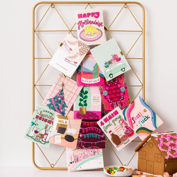 A board with a lot of pink and colorful holiday cards pinned on it in the shape of a Christmas tree.