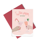 A light pink greeting card with two holiday cocktails clinking and "tis the season bitchessss"