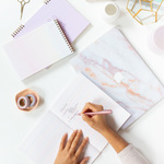 Meltdown washi tape displayed with notebooks and task pads, with a person writing in one of the notebooks with a Rose Gold colored Jotter pen.