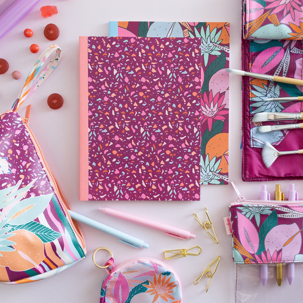 A Terrazzo-speckled notebook and Floral designed notebook surrounded by a Floral nights TOOTsie Roll bag, pixie bag, Dime in bag, and a large Pixie Pouch.