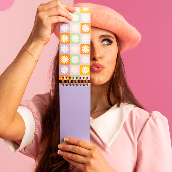 Girl in pink beret holding up a colorful daisy task pad.