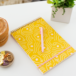 A golden yellow task notebook with a stencil female face design in white lining.