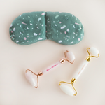 a green weighted eye mask with assorted color terrazzo with two eye rollers on a white background.