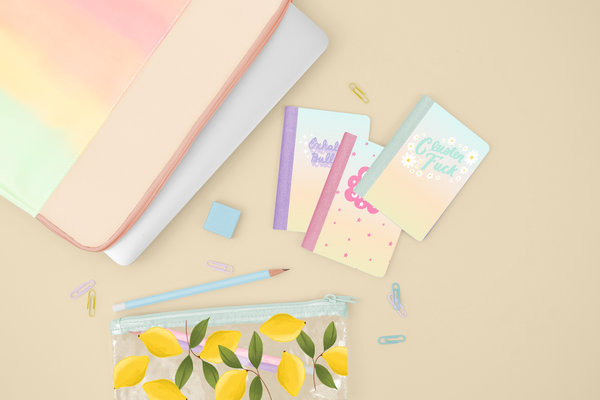 A flat lay of 3 mini notebooks, a ombre rainbow laptop and a lemon pouch. 