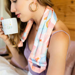 Woman wearing a multicolored, abstract moon designed spa neck wrap. Peach interior color and handles.