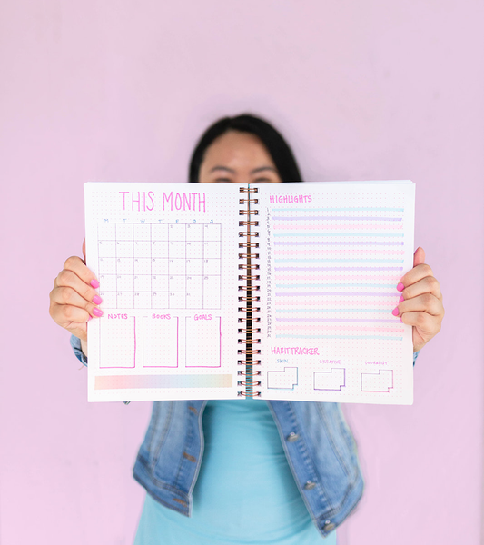 Woman holding up a Far Out Bullet Journal that is opened and has an example layout of how to bullet journal.