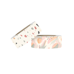 Two rolls of washi tape. The first is white with a  grey, blue, red, yellow and brown terrazzo pattern. The second roll is a watercolored botanical and fruit pattern in light green, corals, orange and pink. 