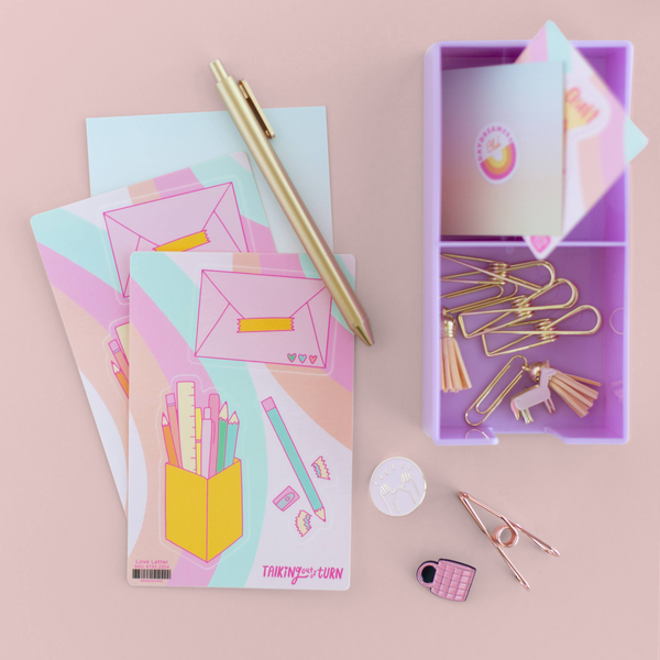 A sticker set with a pink envelope sticker, a pencil sticker, and a stationary set with pencils and pens sticker. Displayed with a lilac Desk Set organizer with more TOOT stickers, a Jotter pen, and paper clips.