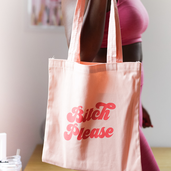 a girl holding Cute canvas tote bag in peach with red Bitch Please lettering design.