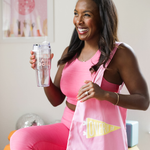 A woman laughing while holding a clear acrylic tumbler printed with "It's all good". She has a pink canvas tote bag on her shoulder with a printed flag and the text "Over It AF"