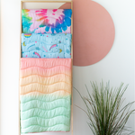 Three puffy quilted blankets in different, multicolored designs, hanging from a blanket rack.