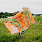 girl running with puffy quilted blanket with big colorful flowers and rainbow swirls with a solid color on the backside