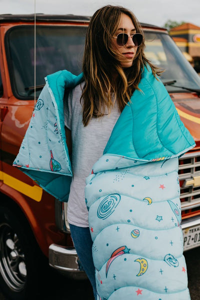 girl with a galactic blanket wrapped around her in front of a van
