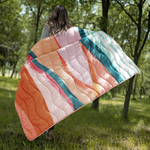 woman running in a field holding puffy quilted blanket in a pastel and teal swirl pattern with solid teal on the backside