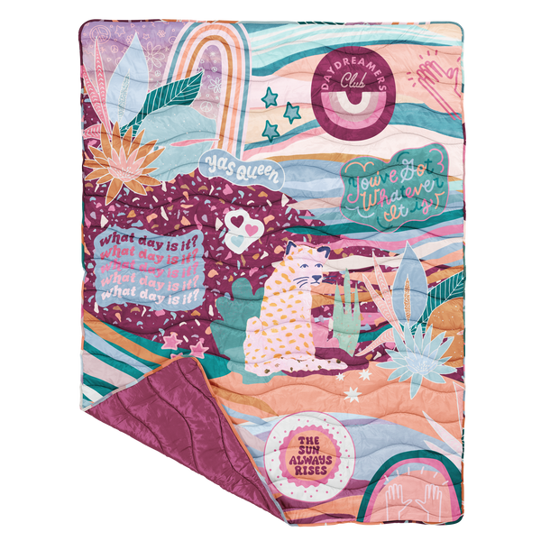 A multicolored, gem-toned terrazzo and succulent printed blanket with a set of hearts, a cat-like animal, and phrases "Daydreamers Club," "You got whatever it is," "The sun always rises," "Yas Queen," and "What day is it?" printed on. Back side is a jewel-toned purple.