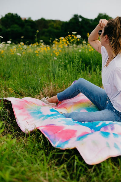 girl sitting in a field on top of a puffy tie dye blanket