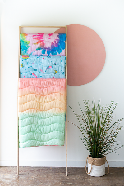Three puffy quilted blankets in different, multicolored designs, hanging from a blanket rack.