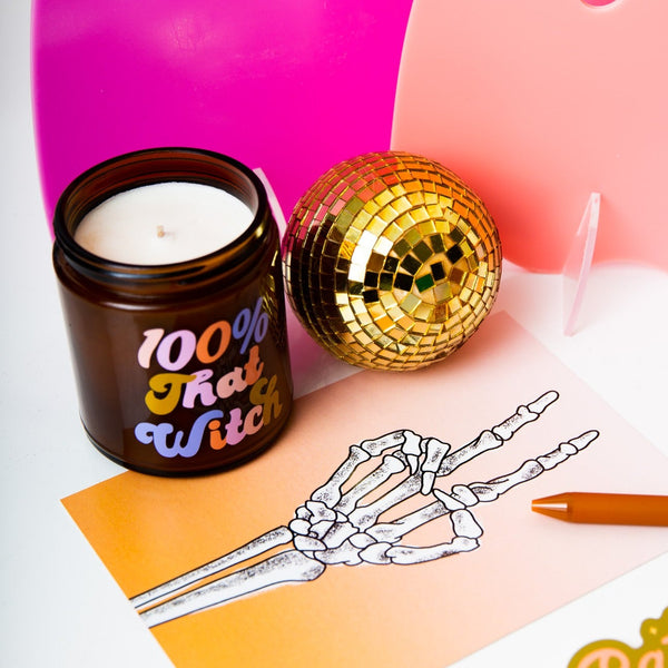 Halloween Candle jar with lid with saying "100% that witch" in shades of pink, purple and orange, small gold disco ball, and skeleton peach sign poster
