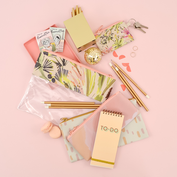A clear vinyl and vegan leather floral zippered pouch surrounded by 2 zippered pouches, a to-do taskpad, gold pencils, enamel pens and a matching coin pouch with keys. 
