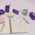 Purple desk set on a table with pens, popcorn, headphones, and coffee.