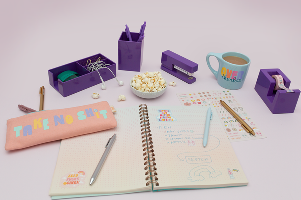 Purple desk set on a table with pens, popcorn, headphones, and coffee. 