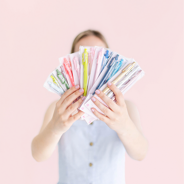 A person holding up all the multicolored Jotter sets in front of a pink background.