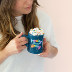 Lady holding blue diner mug that says "Proving them wrong" with whip cream and rainbow sprinkles on top.
