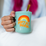 Girl hold a mint diner mug with "Don't be a dick" in shades of orange on the front.
