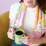 girl holding green coffee mug with colorful flower and swirl printed neck wrap around neck