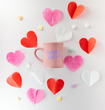 Blush pink diner mug with the words "I fucking love you" on it. The mug is surrounded by pink, red, and white paper hearts, as well as candy conversation hearts.