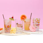 Flower Power Pint Glass Set sitting on a white table and pink background with straws and fruit hanging off of pint glasses.