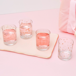 Set of 4 clear glasses with metallic gold print. A bottle of champagne is unopened next to a pink bag.