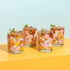 Rocks glass set with flowers in groovy colors with iced tea inside and mint leaves sitting on top.