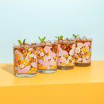 Rocks glass set with flowers in groovy colors with iced tea inside and mint leaves sitting on top.
