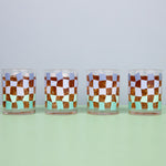 Clear glass cups with a funky checker pattern with a drink inside on a blue background.