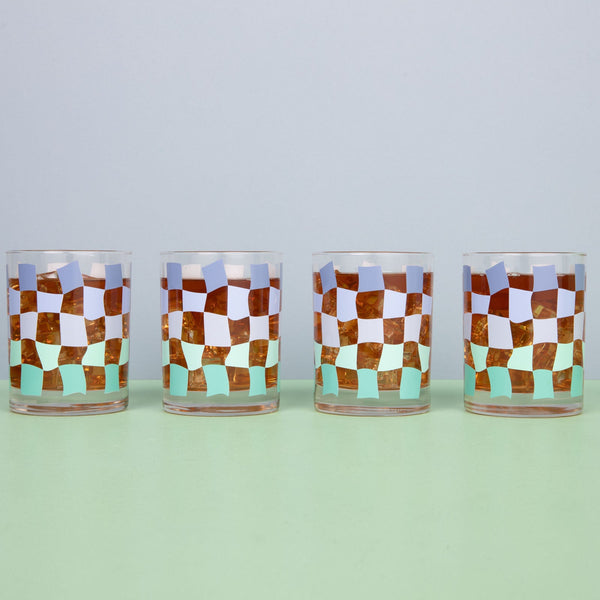 Clear glass cups with a funky checker pattern with a drink inside on a blue background.