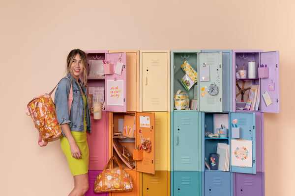 A girl wearing the orange floral everyday backpack next to colorful lockers