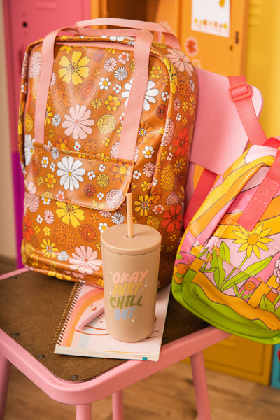 Beige cold cup/tumbler with "okay just chill out" next to an orange floral backpack.